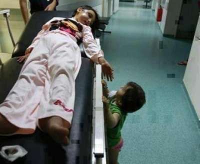 طفـل يحاول تلمـس يـــد اختـه الشهيدة